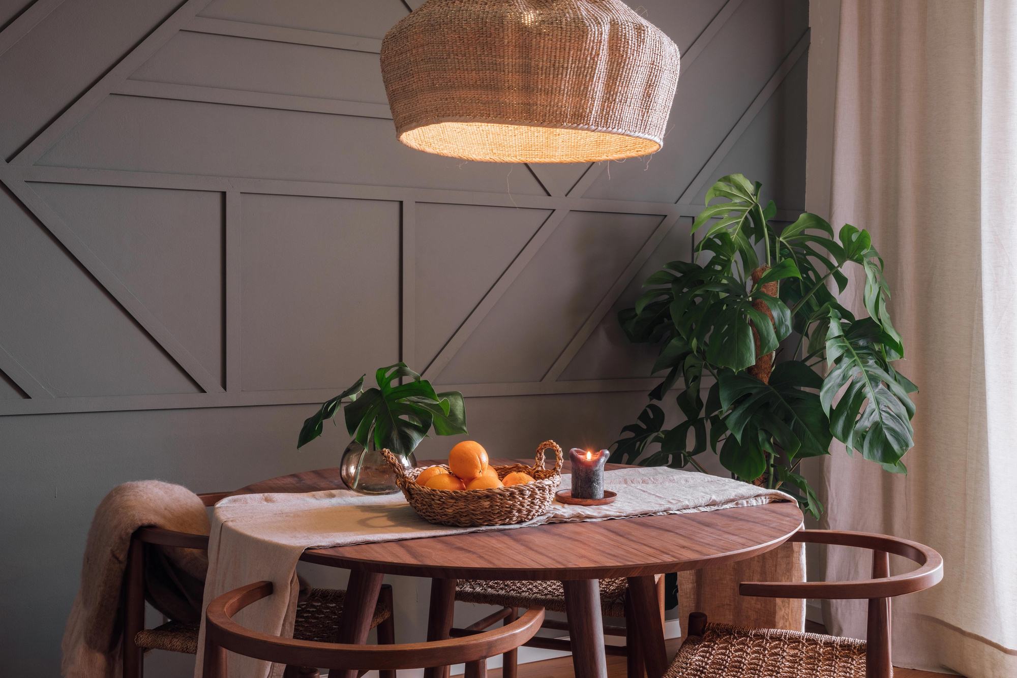 a dining table and chairs in front of a wall. Cozy dining area. Monstera plant, oranges on table, linnen table cloth, beige linnen. Trendy interior setting, interior designer barcelona, Amsterdam, by Aptó interiors