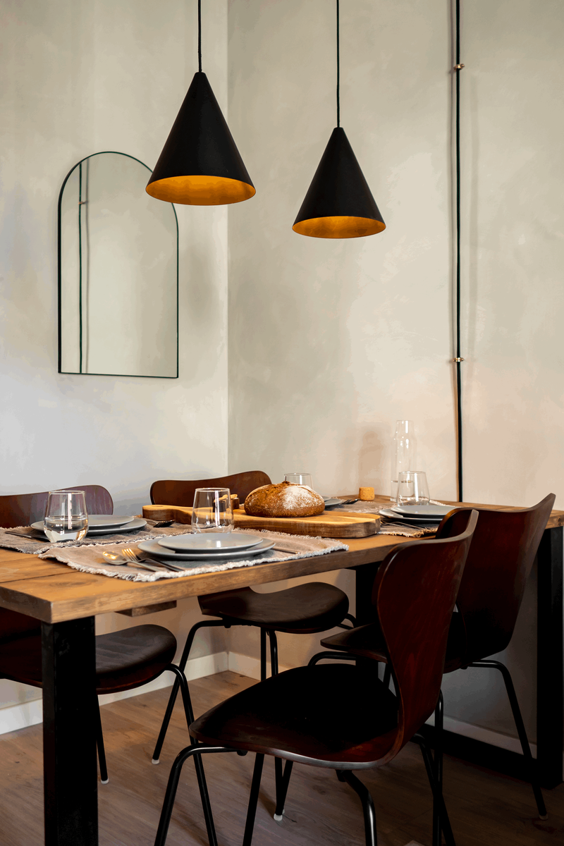 a dining room table with four chairs and two pendant lights. Table setting breakfast, round bread, lime wash wall paint, wall paint effect. Mirror with arch, black hanging table lights, minimalist wooden chairs. By Aptó interiors in Barcelona