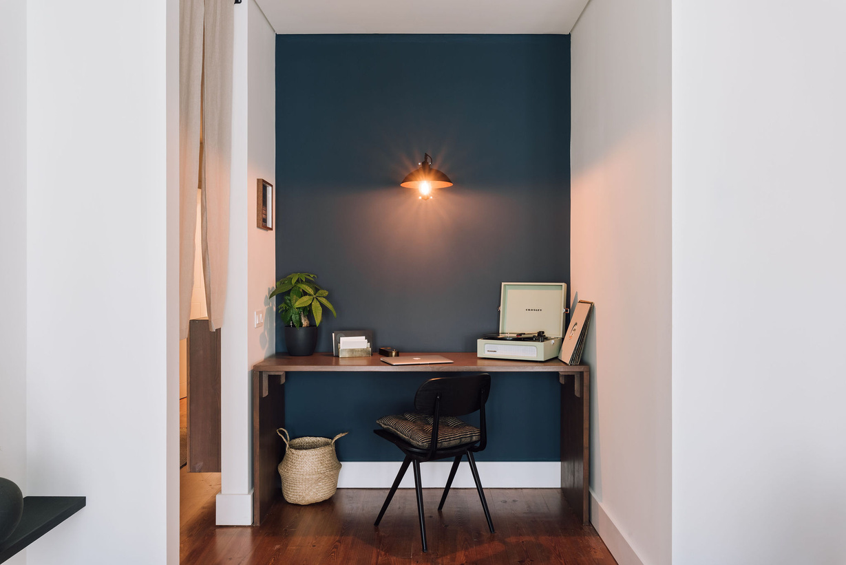 a small office with blue walls and wooden floors. Home office design, wooden desk, old school chair, Crosley cruiser, cosy wall light, Japanese curtains, dark blue walls, marine blue, Japanese inspired design. fladis basket. Aptó interiors