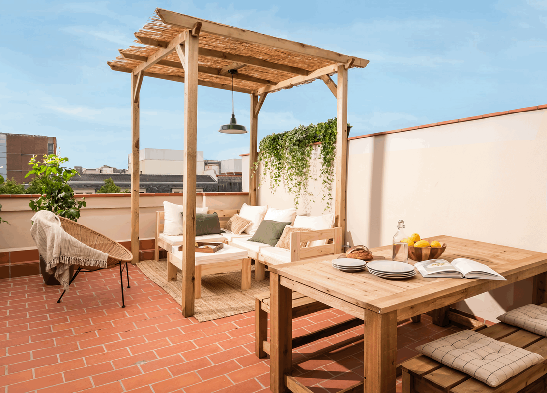 a wooden pergola on the roof of a building with a lounge set and dining table area. Wooden terrace furniture, terrace decoration, summer terrace in Barcelona. Lemons for staging. Home decoration. Interior photoshoot. Zara home, by Aptó interiors