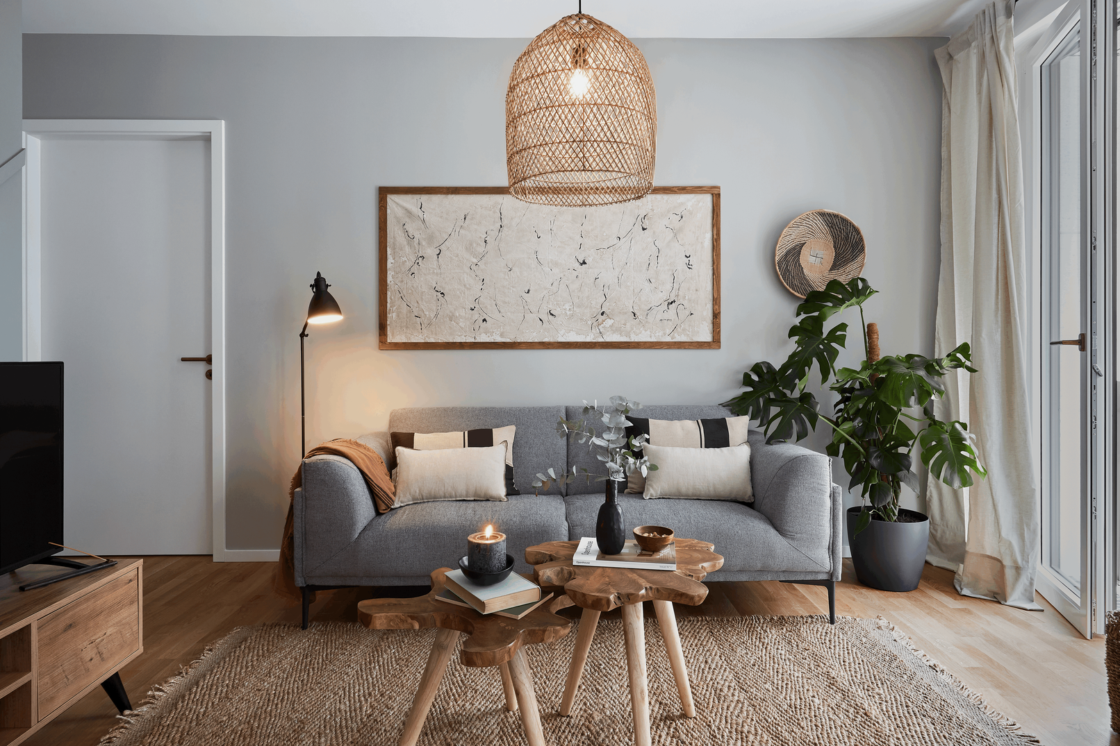 a living room with a sofa, coffee table and rug. Minimalist home, big wall art on wall, striped pillow cases Zara Home, wooden organic tree side tables. Home decoration. Cozy living room. Monstera plant, decorative lamps, candles. Aptó interiors