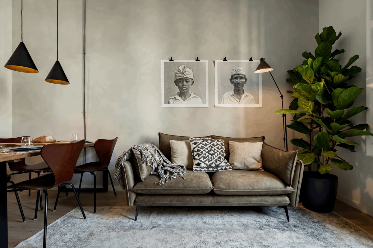 a living room with a couch, table and chairs. Minimalist small table lamps, big fig tree. Interior design. Decoration above sofa, leather sofa, big rug, decorative lights, lime wash wall paint, farrow and ball paint. Aptó interiors Noelle Baartmans
