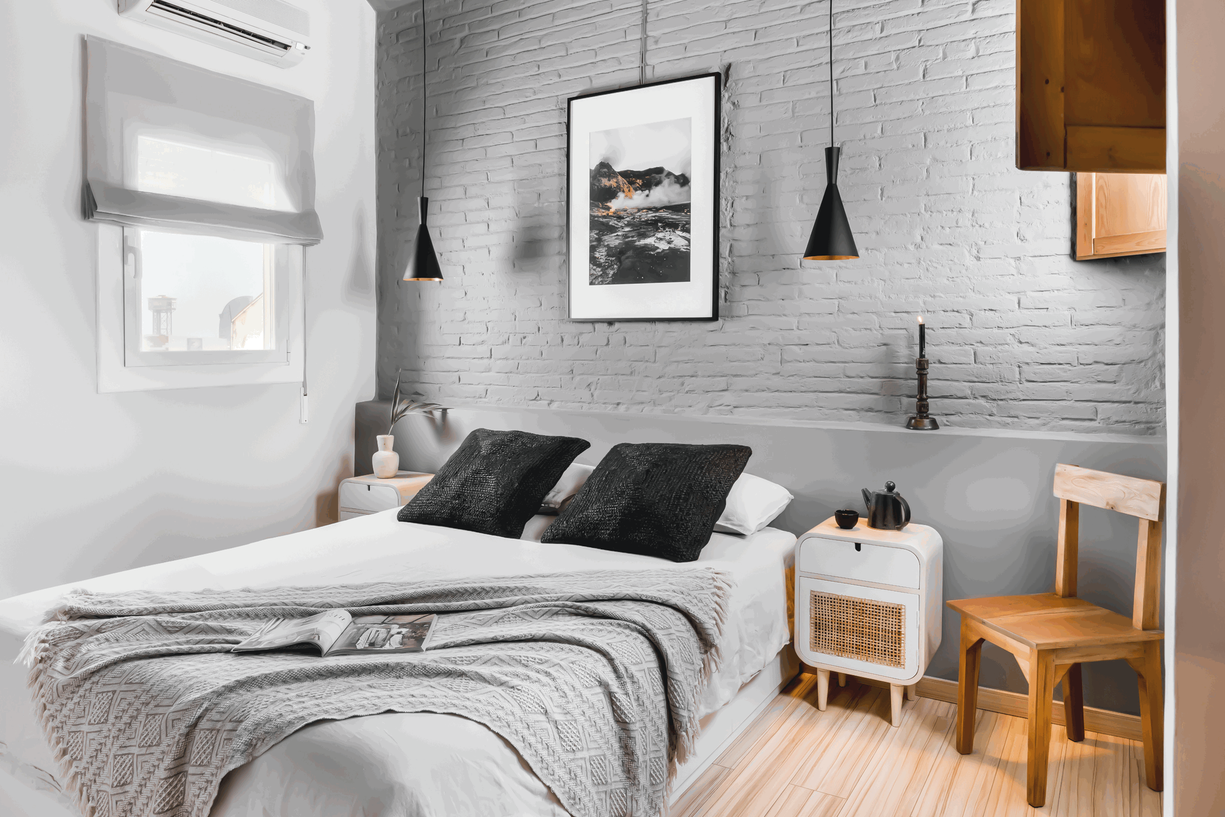 a bedroom with a white brick wall and wooden floors. Grey bedroom design, male bedroom design, minimalist bedroom design, bedroom setting with pillows. Home staging in Barcelona, Amsterdam by Aptó interiors VT wonen 