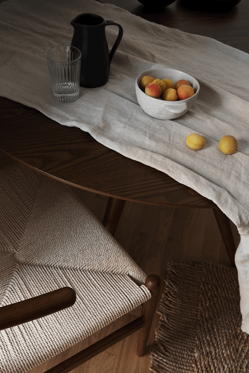 a table with a bowl of fruit and a pitcher of water. Table Setting, linnen table cloth, dark wooden dining table, sklum, have home, zara home, ikea water glasses, jute rug. Kelly wearstler, interior photography styling. by Aptó interiors