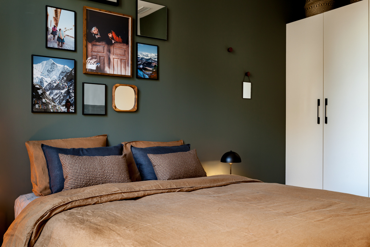 a bedroom with a bed and pictures on the wall. Green walls, olive green wall paint bedroom, Farrow and Ball paint, Terracotta linnen bedsheets, pillows on bed from Zara Home, Zara home design, cozy design. By Aptó interiors
