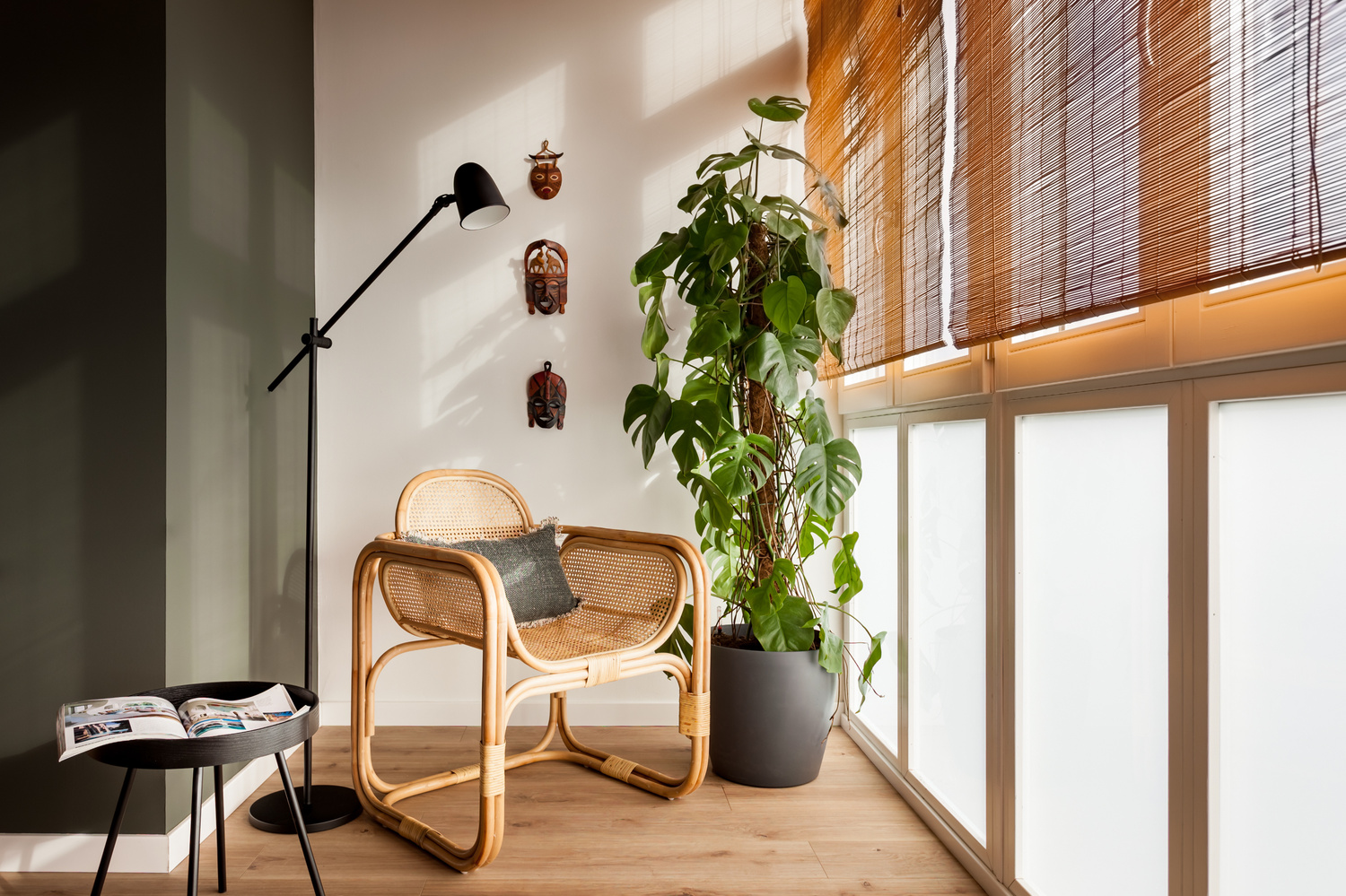 a room with a chair and a plant on the floor. Jungle home design, ethnic interior design, wicker rocking chair, monstera delicious plant, bamboo rolling curtains, interior design for VT wonen, home staging, Aptó interiors, Kelly Wearstler.